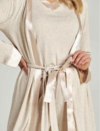 Beżowy, miękki szlafrok z długimi rękawami i satynową lamówką. Posiada wiązany pasek w talii oraz dekolt w serek. Całość ma delikatną fakturę.