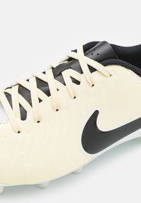 Scarpa da calcio crema e nera con parte superiore in sintetico testurizzato, lacci beige, baffo Nike nero e tacchetti sagomati per la traiettoria.