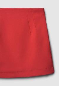 Gonna in tessuto rosso, dalla superficie liscia, con vita aderente, caratterizzata da due pieghe frontali e orlo pulito. Chiusura con zip sul retro.