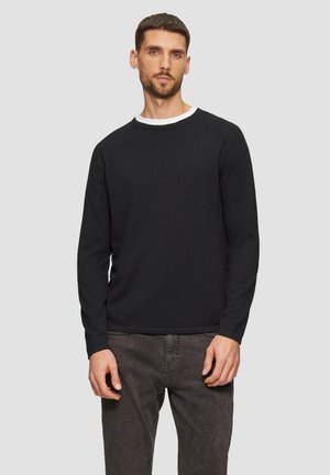 Pull noir à manches longues avec texture côtelée, col rond et col blanc contrastant, associé à un pantalon gris foncé.