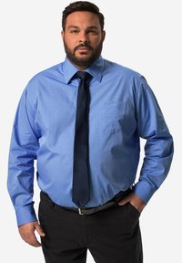 Modrá košile s dlouhým rukávem, s límečkem na knoflíky a kapsou na hrudi, doplněná tmavým krkem a černými kalhotami, s hladkým textilním povrchem.