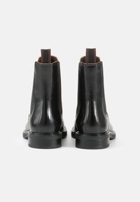 Botas de tobillo de cuero negro con paneles laterales elásticos, tiradores y suela resistente. Textura suave con detalles de costura en contraste.