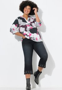 Blouse multicolore avec un motif abstrait gris, rose et blanc, associée à un jean foncé avec des ourlets brodés en scallop et des bottines noires.