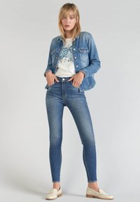Giubbotto di denim azzurro chiaro, maniche lunghe, con bottoni davanti. T-shirt bianca con motivo floreale. Jeans skinny blu scuro. Mocassini color crema.