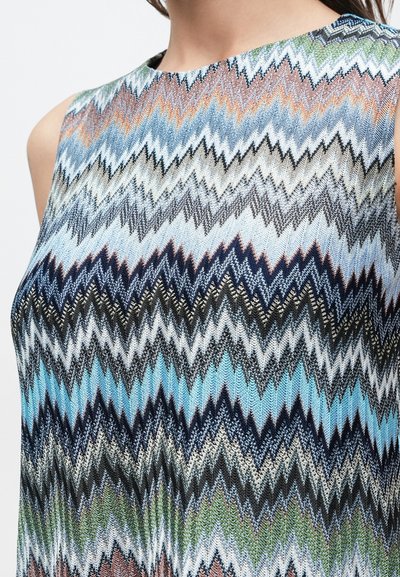 Bezruký top s viacfarebným cikcak vzorom v odtieňoch modrej, zelenej, oranžovej, čiernej a bielej, oblečený osobou zobrazenou od krku nadol.