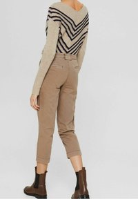 Beige V-ringad tröja med marinblå zigzag-mönster, kombinerad med tanfärgade cropped byxor och bruna ankelstövlar. Texturerad stickning och figursydd design.