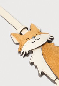 Nahast rebaste võtmehoidja, millel on beež vildist tekstuur, valged nahast aktsendid ja mustad jooned. Omaduseks naeratav nägu ja rihm kinnitamiseks.