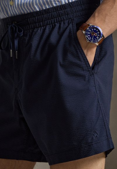 Μπλε σκούρο μαγιό βερμούδα με υφή στο ύφασμα, ελαστική μέση, κορδόνι για ρύθμιση και πλαϊνές τσέπες, με διακριτικό κεντημένο λογότυπο.