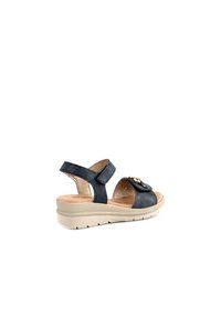 Sandalo in pelle blu navy con cintura sul retro, parte superiore strutturata, accento dorato e suola a zeppa con battistrada decorato per una buona presa.