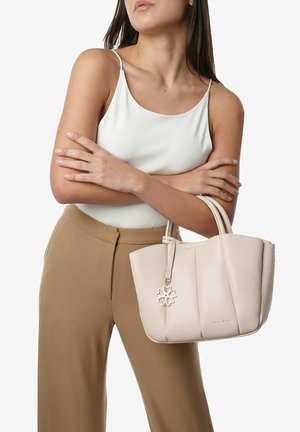 Bolso tote de cuero beige con lados curvados, asas superiores y un charm. Presenta detalles de costura y una textura suave.