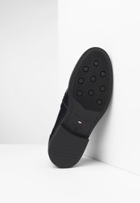 Suela de zapato negra con patrones de tracción circulares, hecha de goma. Presenta el nombre de la marca en relieve y una etiqueta de "Hecho en Italia" en rojo, blanco y verde.