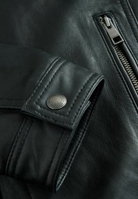 Zwarte leren jacks met een ritssluiting en een drukknopdetail, met zichtbare stikpatronen en een gladde textuur.