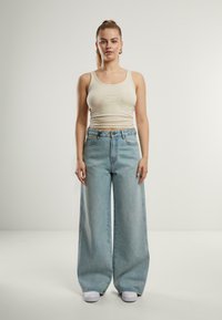 Un maiou ribbed de culoare bej deschis, asortați cu blugi oversized de culoare bleu deschis. Tenisi albi completează ținuta. Design simplu, croială lejeră.