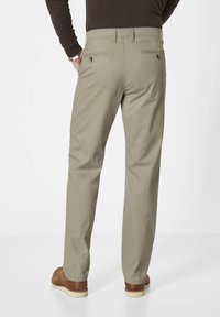 Beige Baumwollhosen mit geradem Schnitt, ausgestattet mit zwei Gesäßtaschen mit Knopfverschlüssen, getragen mit braunen Lederschuhen.