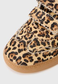 Tenisky s leopardím vzorom, ktoré majú štruktúrovaný vrch z pony hair, suchý zips a gumovú podrážku so zúbkami.