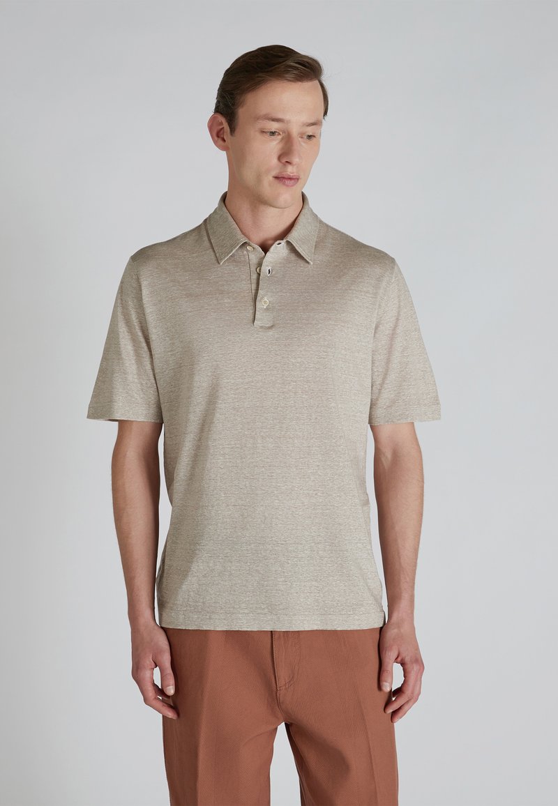 Beżowa koszulka polo z krótkim rękawem o teksturowanym wykończeniu, z zapięciem na dwa guziki i klasycznym kołnierzykiem, w zestawieniu z spodniami w kolorze rdzy.