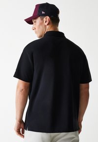 Black polo shirt with a solid design, short sleeves, and side slits. Paired with a two-tone cap, burgundy and black mesh.