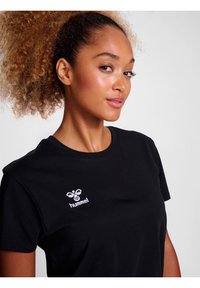 Tricou negru din bumbac, cu guler rotund și mâneci scurte, având un logo alb brodat în zona stângă a pieptului.