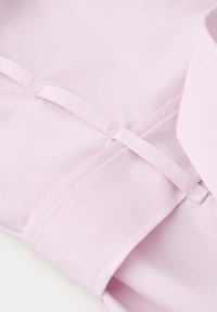 Gros plan sur un tissu rose clair avec des coutures soignées et un petit détail de boucle en tissu sur un vêtement.