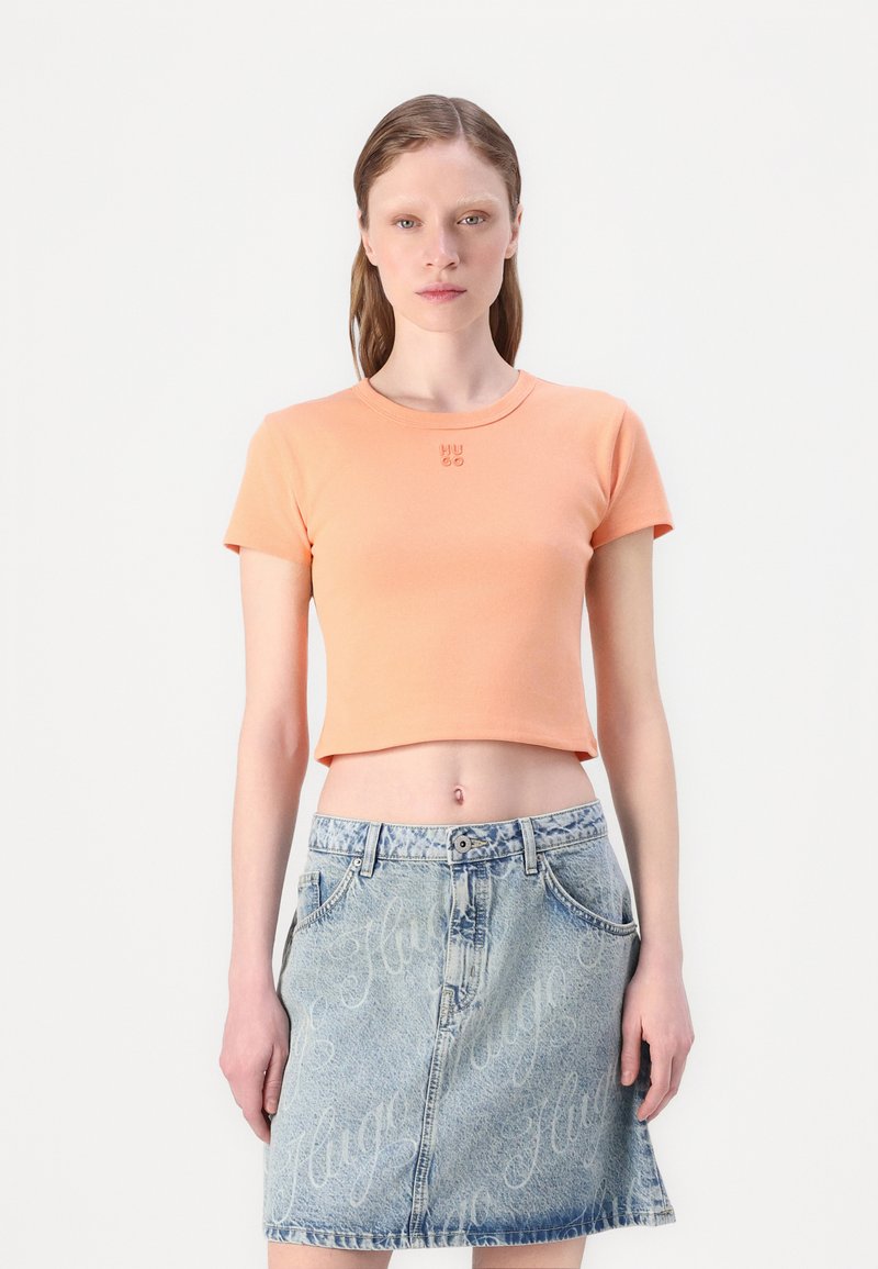 T-shirt cropped pêche à manches courtes avec le logo "HUGO". Associé à une jupe en denim bleu clair avec un motif de logo subtil et des poches.
