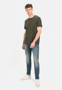 Oliven grøn bomulds T-shirt med rund hals, parret med lyseblå denim jeans og hvide sneakers. Afslappet, tætsiddende silhuet; minimal branding.