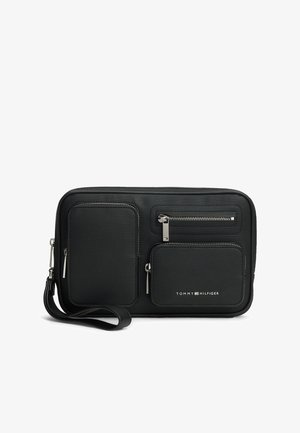 Pochette rectangulaire noire avec trois poches zippées et logo Tommy Hilfiger à l'avant.