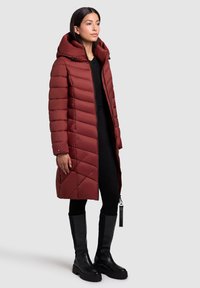 Bordo pernata jakna s kapuljačom, prošivenim uzorkom, prednjim zatvaračem i bočnim džepovima. Nošena preko crne odjeće i u kombinaciji s crnim čizmama.