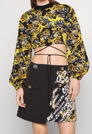 Krótkie, długie rękawy z żółtym barokowym nadrukiem i napisem "Versace Couture" zestawione z czarną mini spódniczką z kieszenią i wzorzystym panelem.