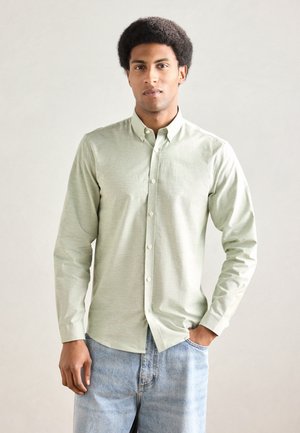 Hellgrünes, langärmeliges Hemd mit Knöpfen, Kragen, texturierter Stoff und abgerundetem Saum. Kombiniert mit hellblauen Jeans aus Denim.