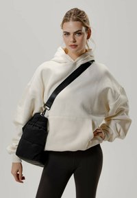 Ylipitkä kermahuppari, jossa on etutasku, yhdistettynä tiukkoihin mustiin leggingsseihin ja tikattuun mustaan olkalaukkuun, jossa on musta hihna.