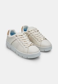Baskets blanches avec un dessus en cuir lisse, des accents en daim à l'arrière, des lacets plats et une semelle en caoutchouc texturée. Design minimaliste avec des perforations.