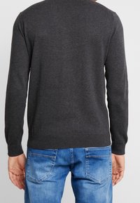Dunkelgrauer gestrickter Pullover mit langen Ärmeln, rundem Hals und geripptem Saum. Über hellblauen Jeans getragen.