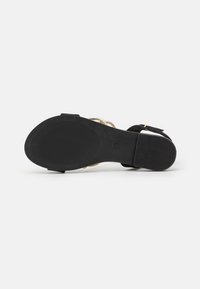 Black suede sandal with a textured sole, metallic gold straps, an ankle buckle, and a modest heel for support and stability.