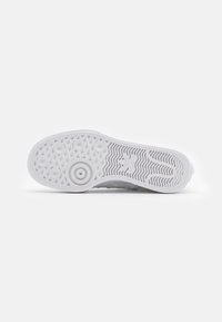 Bílé podešev tenisky se zaoblenými a vlnitými vzory, logo Adidas a texturované gripové plochy na bílém pozadí.