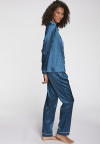 Satin nachtblaues Schlafanzug-Set mit langen Ärmeln und geraden Hosen, mit weißen Paspeln und Knöpfen auf der Vorderseite. Weiche, glatte Textur.