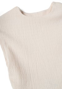 Tela texturizada beige con un patrón arrugado, que muestra la parte superior y el escote redondo de una prenda sin mangas.