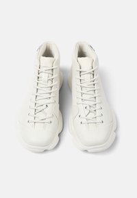 Białe sneakersy za kostkę wykonane z gładkiej skóry, z teksturowanym językiem, zaokrąglonym noskiem oraz płaskimi sznurówkami, posiadające amortyzującą podeszwę.