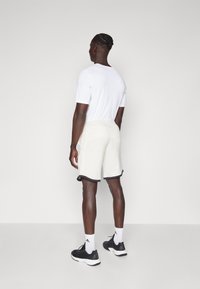 Light gray, soft fabric shorts with a black hem, paired with a plain white t-shirt and black athletic shoes, viewed from the back.