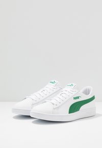 Baskets blanches en cuir lisse, avec une bande latérale verte, un design à lacets, et un col rembourré pour le confort.