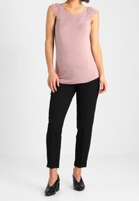 Světle růžový bezrukávový top s krajkovými detaily na ramenech, doplněný o černé slim fit kalhoty a černé vysoké podpatky. Jednoduchý, moderní design.