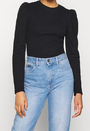 Personne portant un haut noir ajusté à manches longues avec des épaules bouffantes et un jean bleu clair taille haute avec des poches à l'avant.