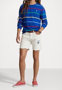 Camisa de manga larga azul con rayas multicolores, pantalones cortos de denim blancos con bajo deshilachado y desgastes, zapatos rosas con suelas blancas.