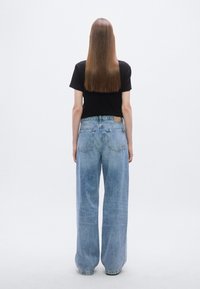 T-shirt noir associé à un jean large bleu clair. Le jean présente un design de poche arrière et une petite étiquette sur la ceinture.