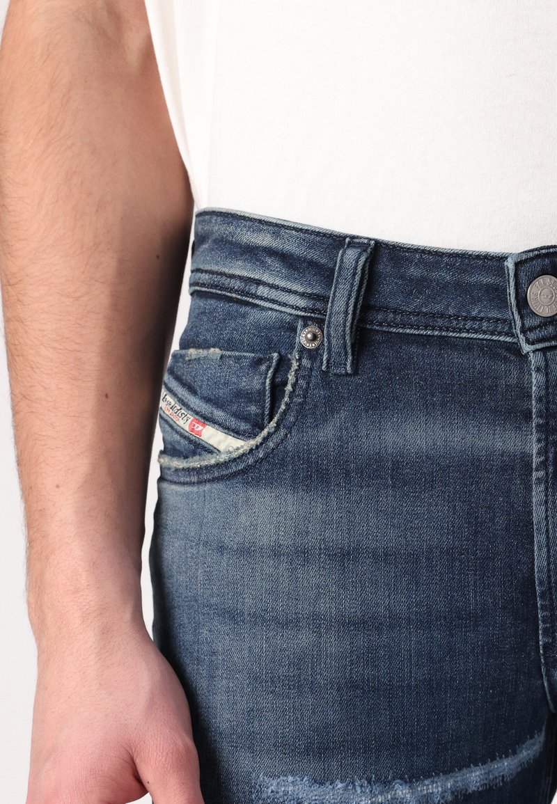 Donkerblauwe spijkerbroek met een klassieke pasvorm, voorzien van een voorzak met een merketiket en een zilveren knoopaccent.