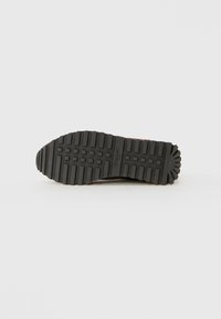 Semelle en caoutchouc noire d'une chaussure avec un motif de crampons profond et le branding "Blauer USA" centré, présentée sur un fond blanc uni.