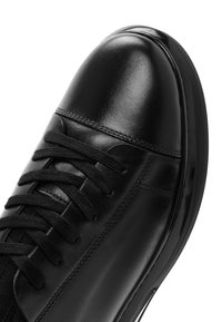 Sneaker in pelle nera con finitura lucida, dotato di sei lacci neri, punta arrotondata e pannello laterale testurizzato.