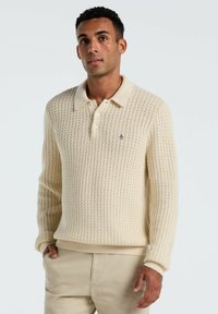 Cremfarbener Strickpullover mit strukturiertem Muster, langen Ärmeln und Kragen. Verfügt über ein kleines Logo auf der Brust.