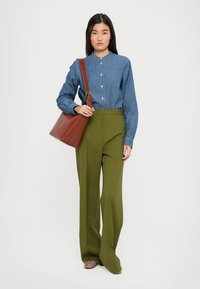 Camicia in denim con bottoni, maniche lunghe, abbinata a pantaloni ampi a vita alta di colore verde oliva. Borsa marrone e sandali a strisce multicolori.