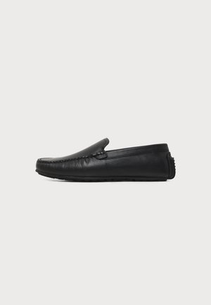 Schwarzer Leder-Slipper mit genähter Oberseite und strukturierter Sohle, seitlich auf einem schlichten hellen Hintergrund gezeigt.