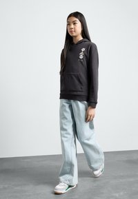 Sweatshirt preto com bordado floral e bolso canguru, combinado com jeans de perna larga azul claro e ténis brancos com detalhes verdes.